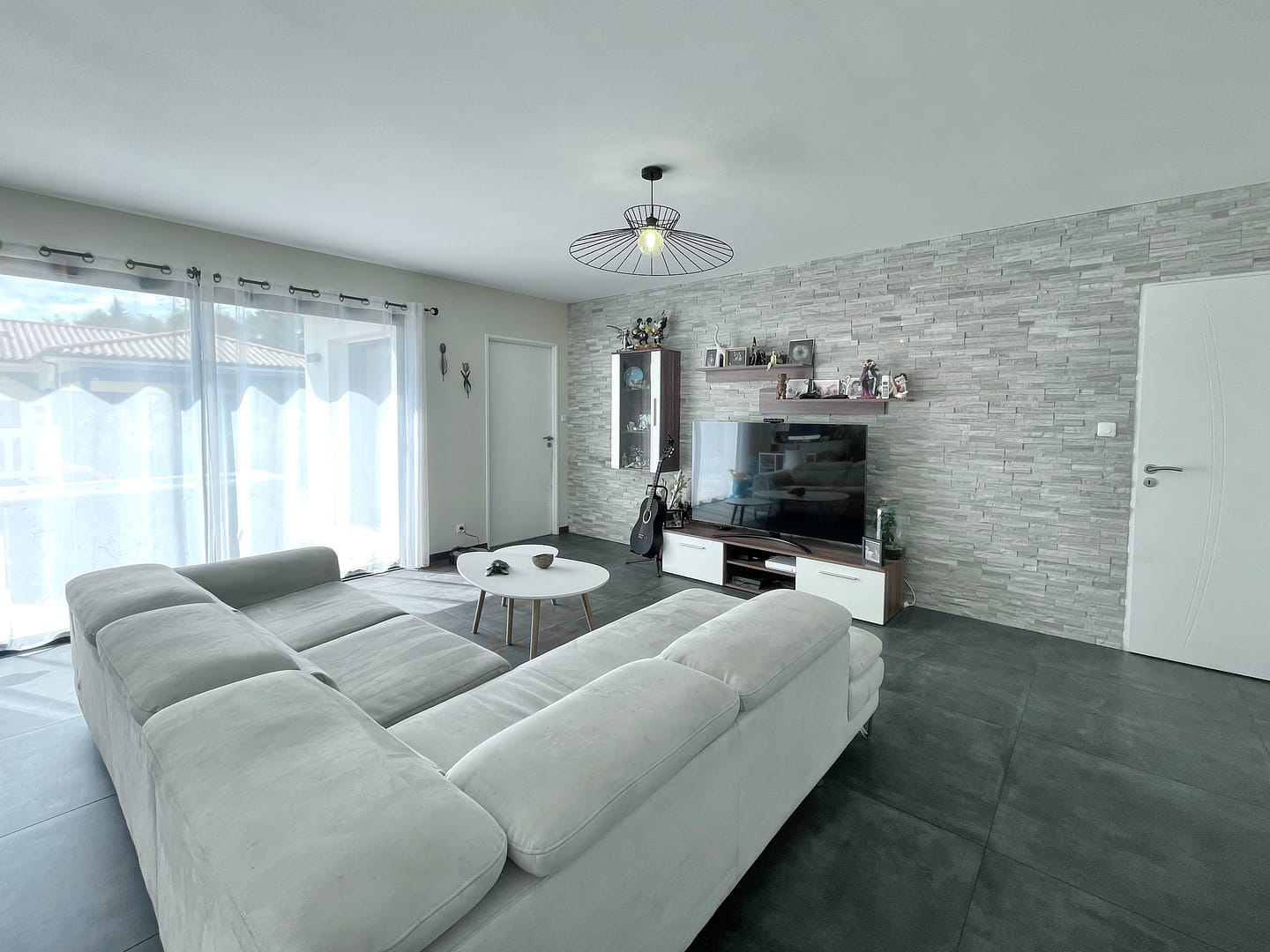 Salon moderne lumineux, canapé gris, mur en briques